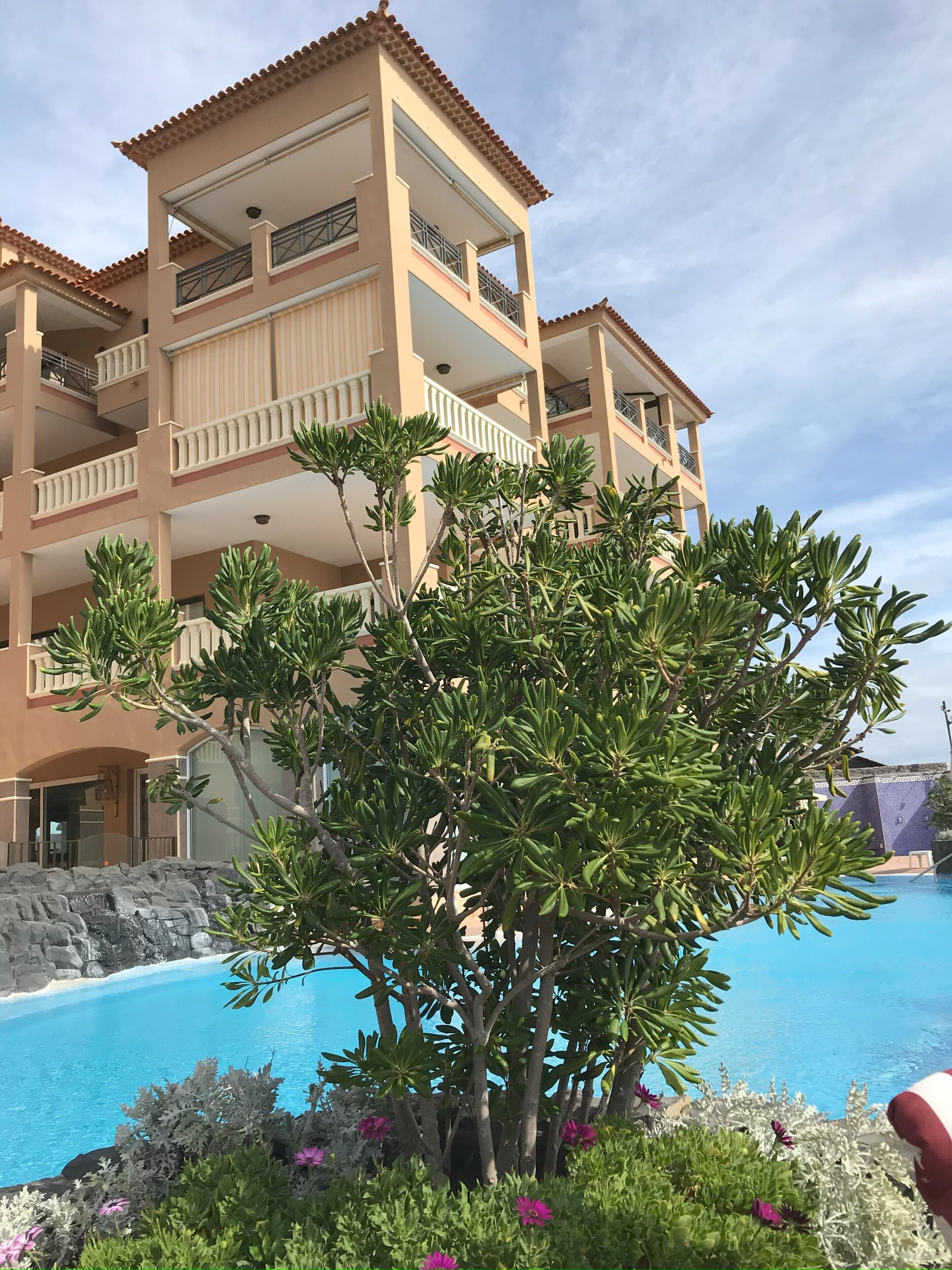 A multi-story hotel with balconies, a swimming pool, and surrounding greenery.
