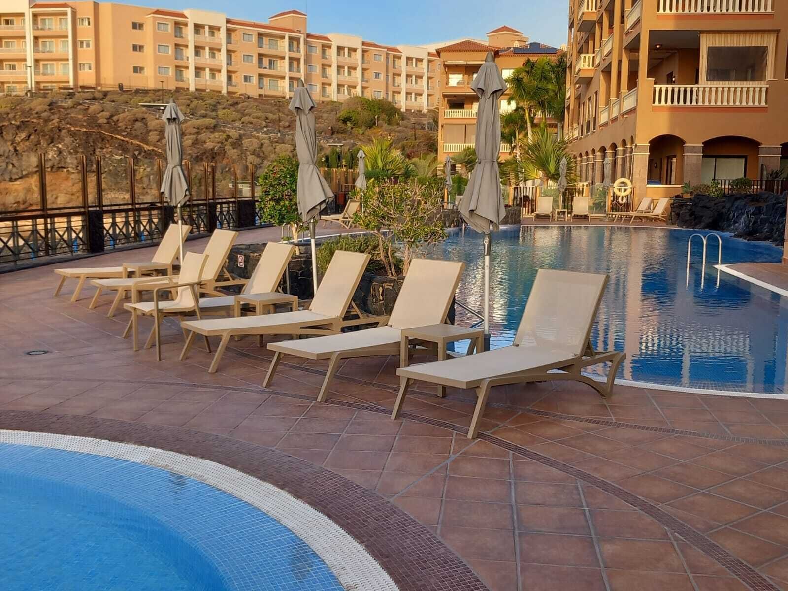 A pool area with lounge chairs and umbrellas, surrounded by a hotel building with balconies.