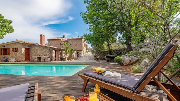 Une terrasse en bois avec une piscine, des chaises longues et un plateau contenant des boissons et des fruits.