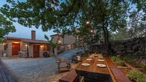 Un espace extérieur aménagé pour les repas, avec une terrasse en pierre, du mobilier en bois et un bâtiment en pierre en arrière-plan.