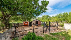 Une clôture en bois rustique, un mur de pierres et un petit bâtiment en bois doté d’un toit en pente.