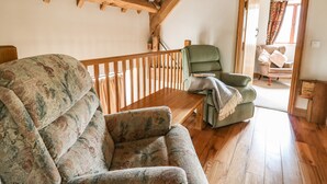 Une pièce chaleureuse avec un plafond en bois, un canapé à motifs, un fauteuil vert et un banc en bois.