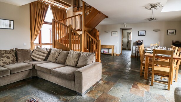 Un vaste espace de vie agrémenté d’un escalier en bois, d’une table à manger pour quatre personnes et d’un grand canapé d’angle.