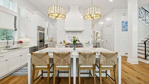 A spacious kitchen with white cabinetry, a large island with bar stools, and pendant lighting. - President`s Row in WaterColor with Heated Pool, LSV, Bikes! STEPS to BEACH CLUB! RENOVATED 2025! (Santa Rosa Beach)