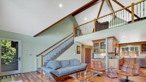 Un vaste espace de vie agrémenté d’un escalier en bois, d’un canapé, d’une table basse en verre et d’un fauteuil en cuir.