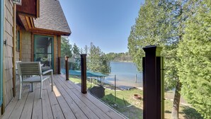 Une terrasse en bois offrant une vue sur un lac, un espace salon couvert et un bâtiment avec une porte verte.