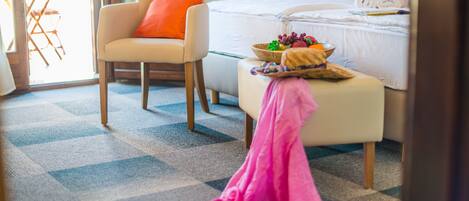 A hotel room with a bed, a chair, a small table with fruit, and a pink towel on the floor.
