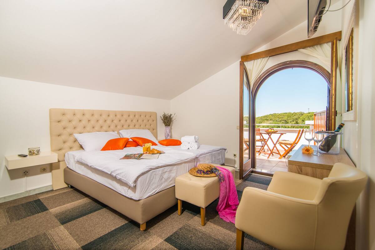 A bedroom with a large bed, a bedside table, a chair, and a view of the outdoors.