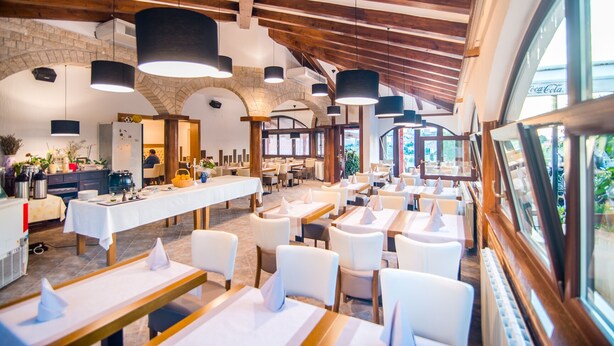 Un restaurante con un interior rústico, que presenta vigas de madera a la vista, paredes de piedra y una larga mesa común con manteles blancos.