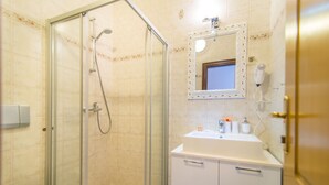 Un baño con ducha de vidrio, inodoro, lavamanos con espejo y secador de pelo en la pared.
