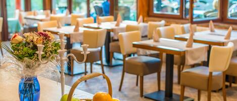 A restaurant interior with tables, chairs, and a vase with flowers and fruit.