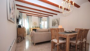 Un salón acogedor con sofá, mesa de comedor de madera y sillas. Cuenta con chimenea, candelabro y obras de arte en las paredes.