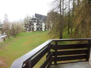A multi-story residential building with balconies, surrounded by a grassy area and trees.