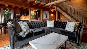 A cozy living room with a sectional sofa, a marble coffee table, and a staircase with a wooden railing. - Mountain View Sanctuary | Pet-Friendly Weaverville Log Cabin | Hot Tub & Long-Range Views (Weaverville)