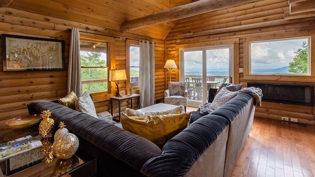 A log cabin interior with a sofa, armchair, and table. - Mountain View Sanctuary | Pet-Friendly Weaverville Log Cabin | Hot Tub & Long-Range Views (Weaverville)
