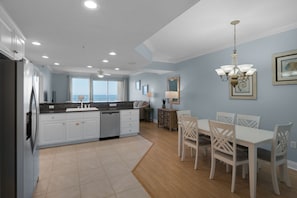 A modern kitchen with white cabinets, a built-in dishwasher, and a large window offering a view of the ocean.