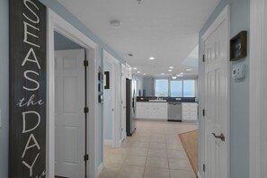 Stunning ocean views await through large windows in this inviting hallway leading to a kitchen with white cabinetry and a sink.