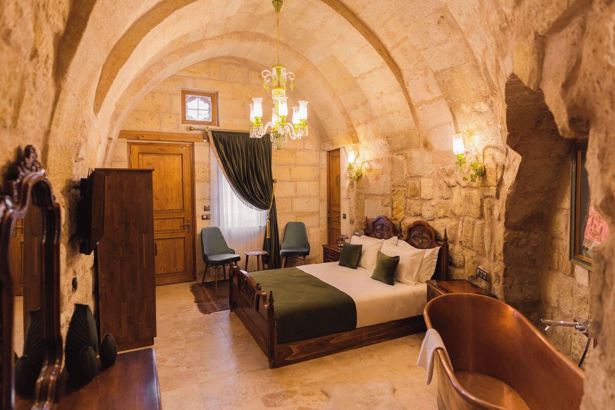 A stone-walled bedroom with a wooden bed, a clawfoot bathtub, and a chandelier.