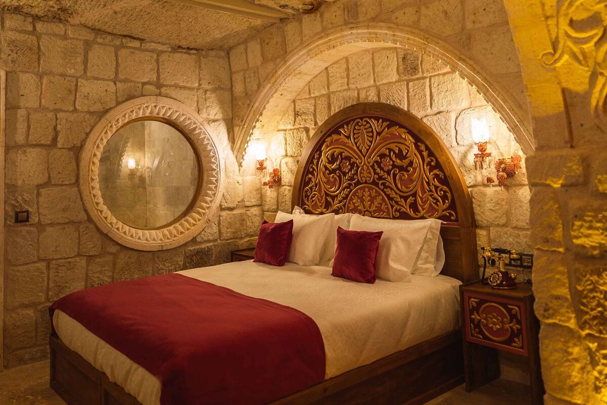 A stone-walled bedroom with a wooden bed, a round mirror, and a decorative headboard.