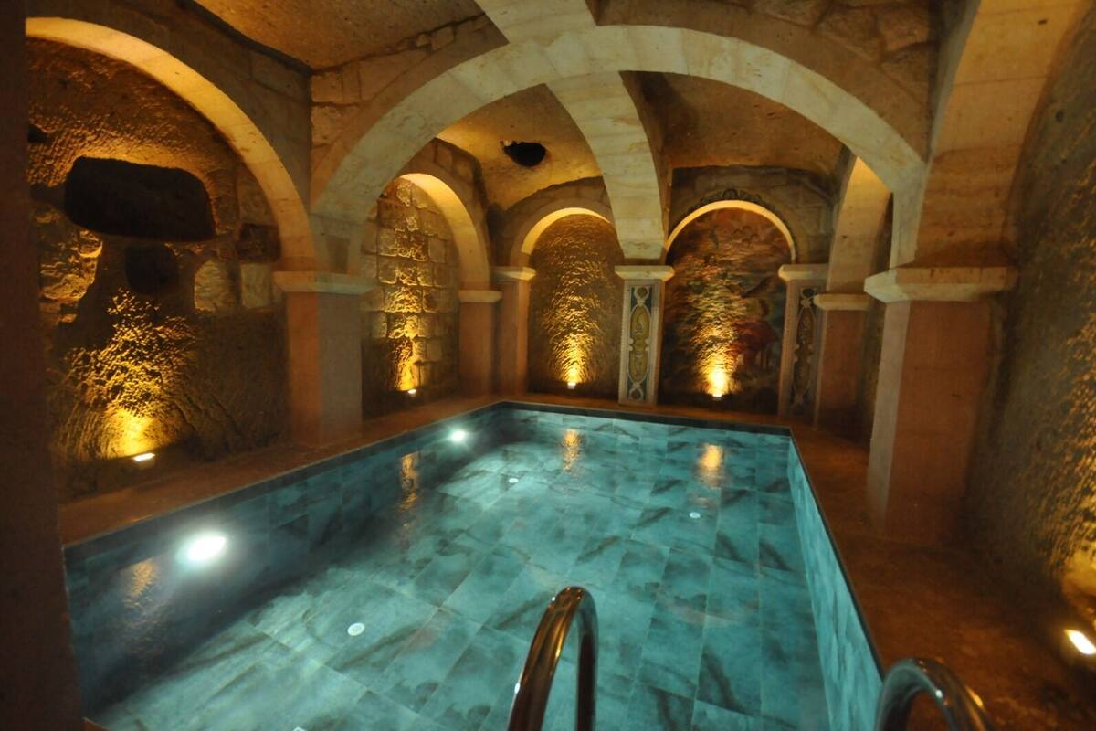 A swimming pool with stone walls and arches, illuminated by warm lighting.
