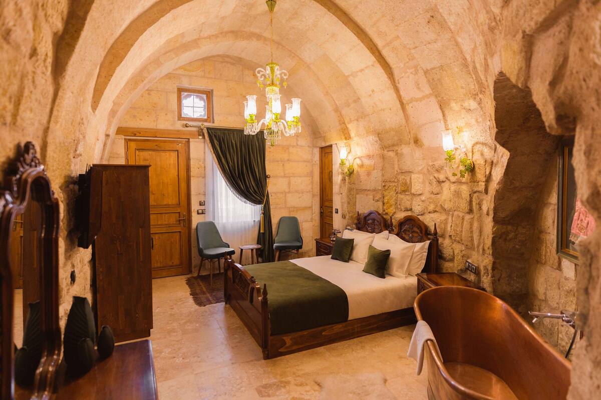 A stone-walled bedroom with a wooden bed, a clawfoot bathtub, and a chandelier.