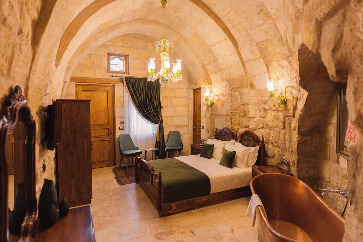 A stone-walled bedroom with a wooden bed, a clawfoot bathtub, and a chandelier.