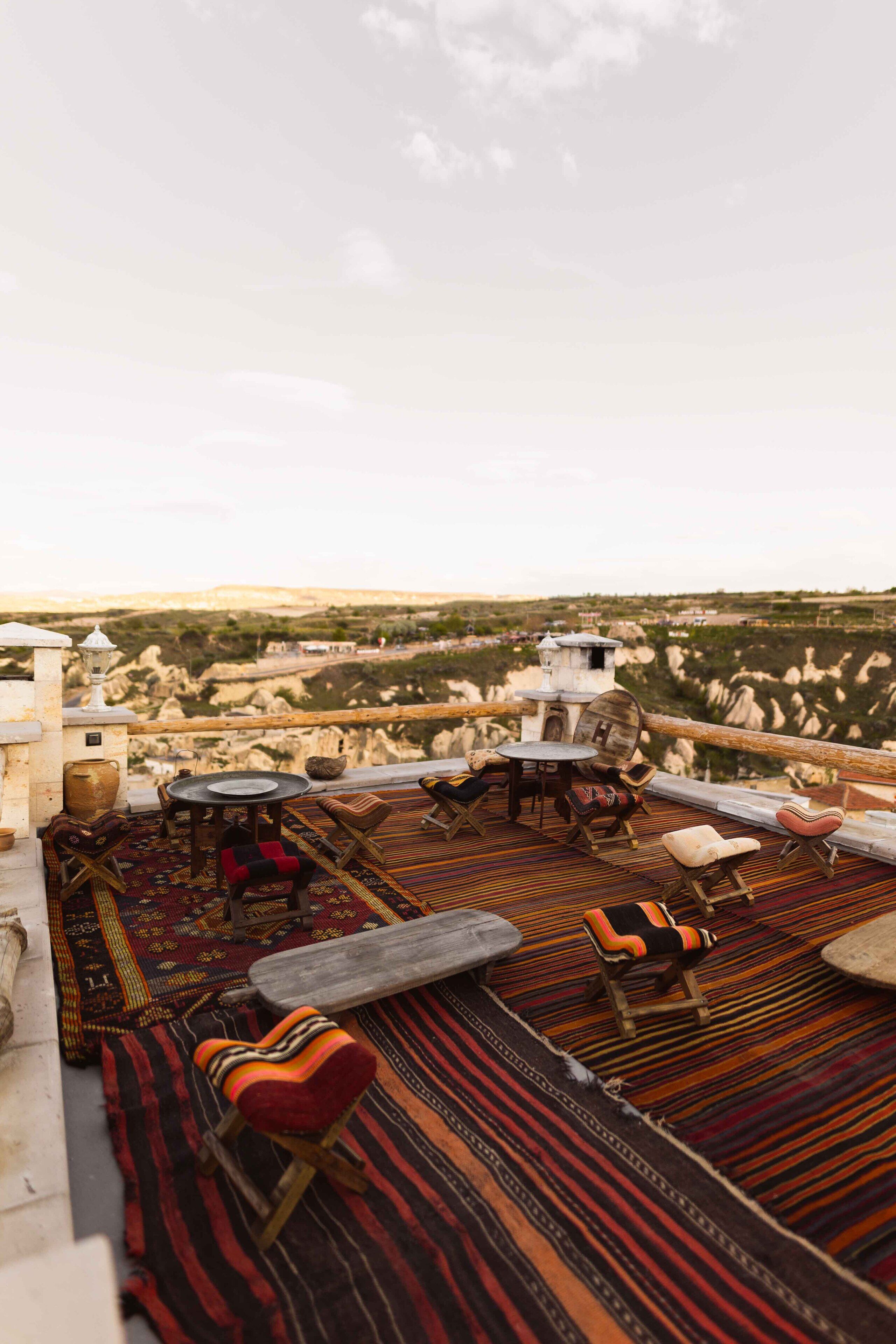 A rooftop terrace with a view of a rugged landscape, furnished with a table, chairs, and a small lamp.