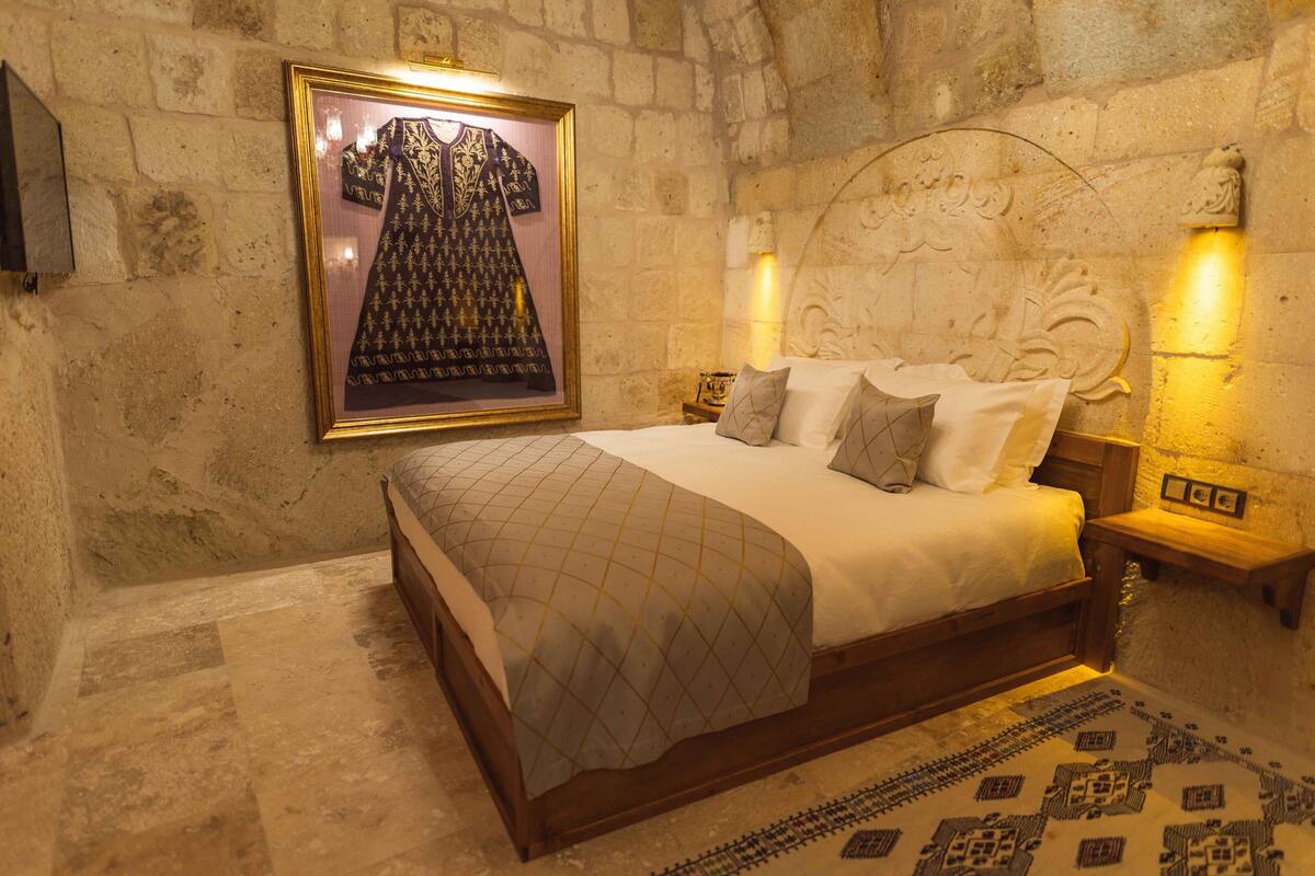 A bedroom with a bed, a framed tapestry, and a stone wall.