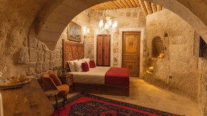A stone-walled bedroom with a bed, a chandelier, and a wooden door. - Solo Cave Suites (Ürgüp)