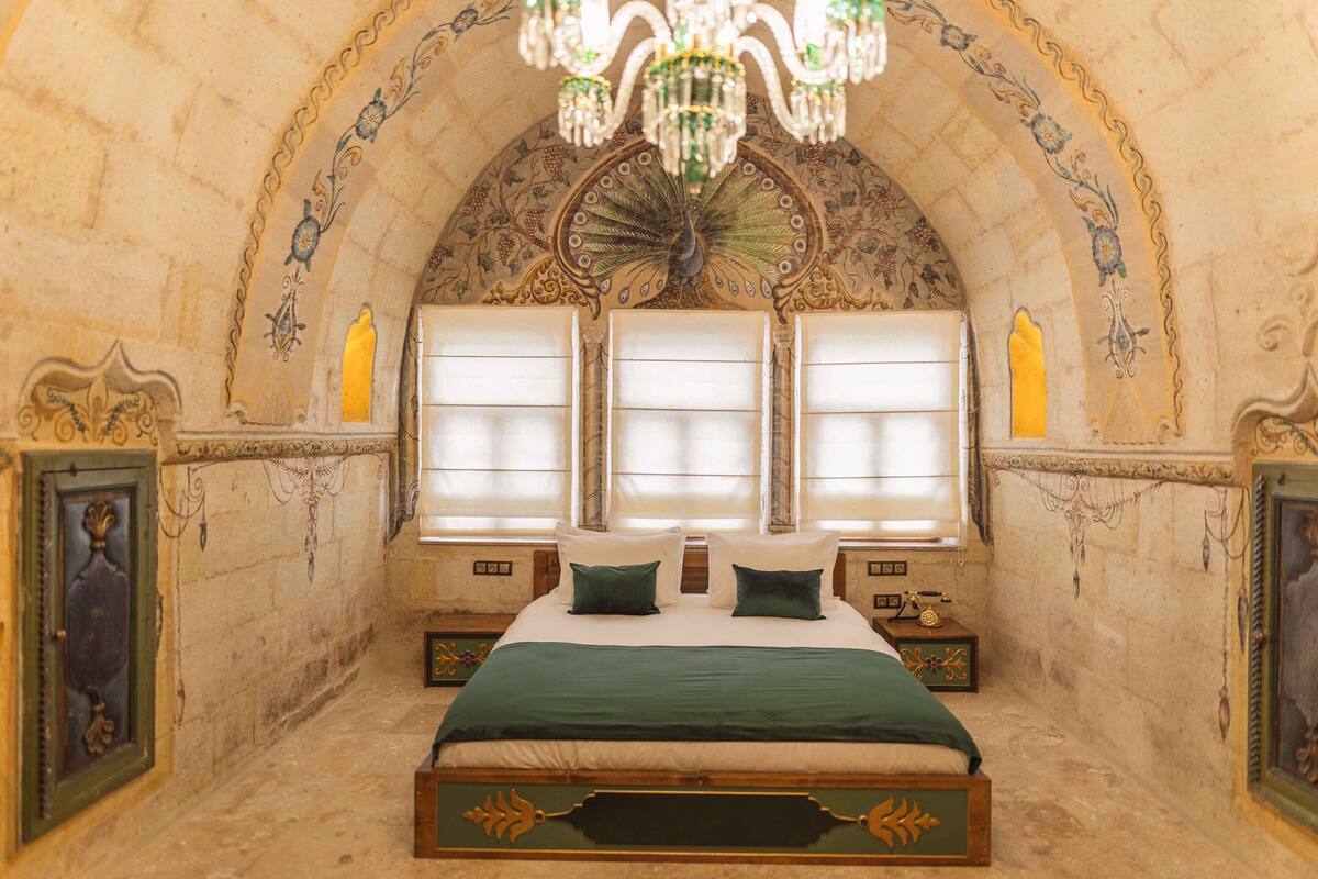 A bedroom with a large bed, ornate ceiling, and a chandelier.