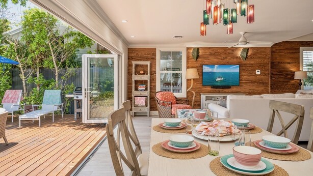 A modern living room with a wooden accent wall, a television, and a dining area set up for a meal. - **SOUTHERNMOST BLISS @ OLD TOWN** Home & Pool + Last Key White Glove Service... (Key West)