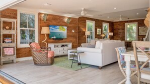 A spacious living room with a white sofa, a wicker chair, a TV mounted on a wooden wall, and a bookshelf. - **SOUTHERNMOST BLISS @ OLD TOWN** Home & Pool + Last Key White Glove Service... (Key West)