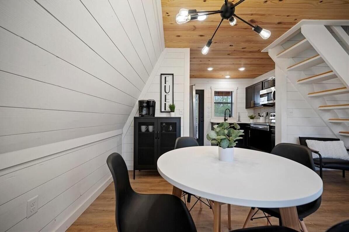 A modern kitchen with white cabinetry, a dining area with a round table and chairs, and a staircase with wooden steps.