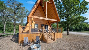 A wooden cabin with a balcony, a fire pit, and a staircase leading to the upper level.