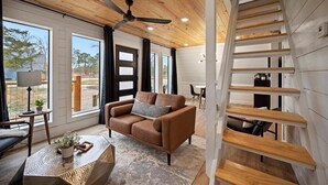 A modern interior with a wooden ceiling, a brown sofa, a dining table, and a spiral staircase.
