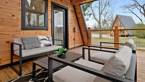 A wooden cabin with a sloped roof, a sofa, a coffee table, and a view of the surrounding landscape. - “Elk” High LUXE 1 Bedroom A-Frame, The Alps of Hochatown (Broken Bow)