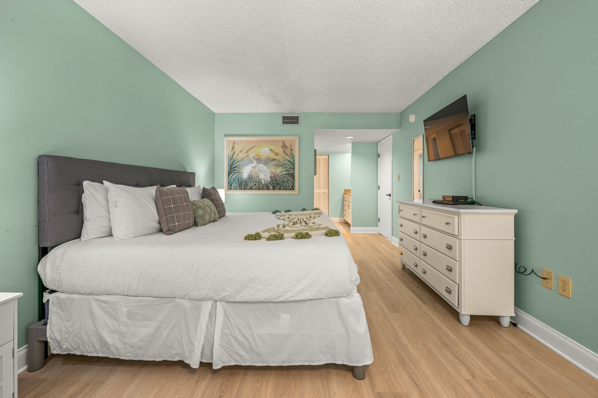 A bedroom with a large bed, a dresser, and a painting on the wall.
