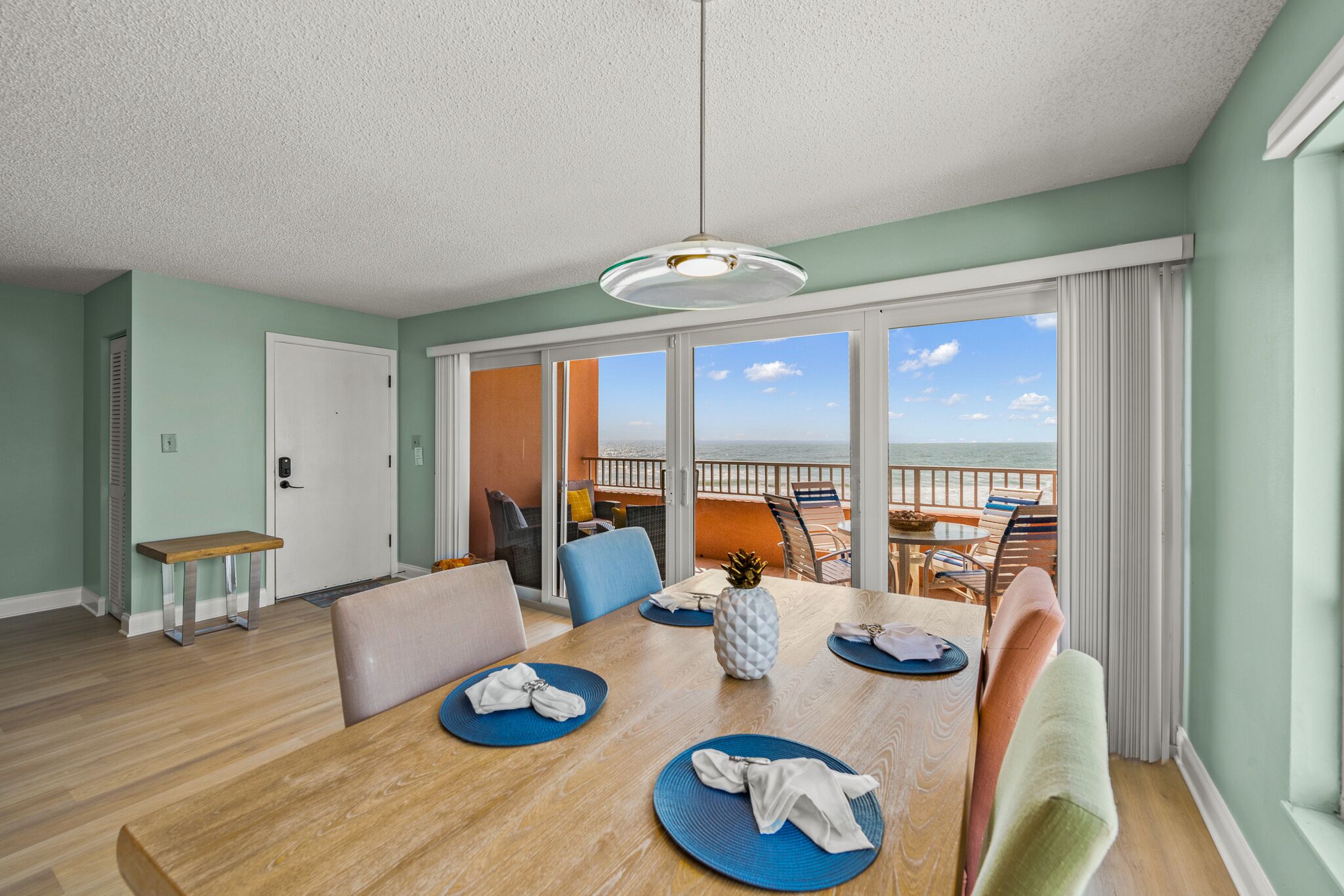 A dining area with a wooden table, blue placemats, and chairs. There is a view of the ocean through large windows.