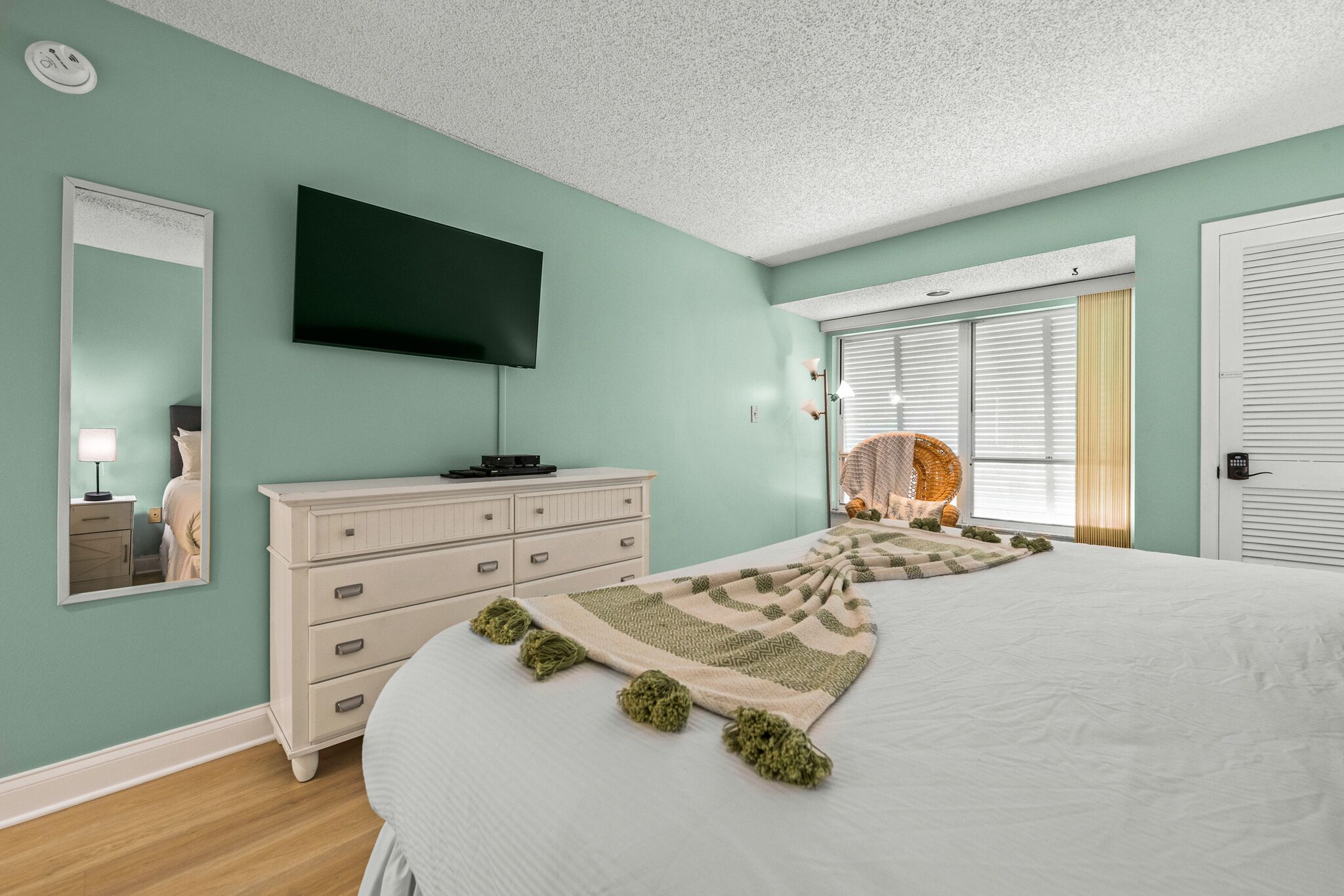 A bedroom with a bed, dresser, mirror, and a flat-screen TV.