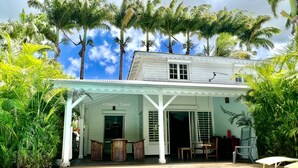 Un edificio blanco con un patio cubierto, piscina y palmeras al fondo.