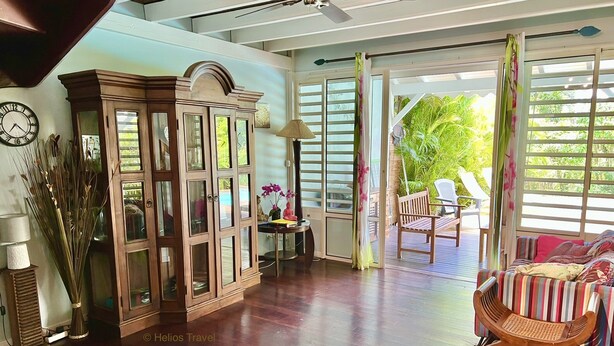 Una habitación amplia con piso de madera, ventilador de techo, un mueble, una silla y vistas al exterior a través de una puerta corrediza.