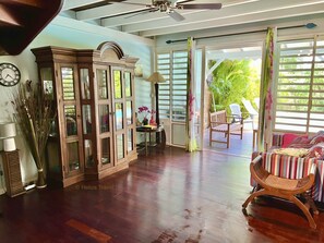 Um quarto espaçoso com piso de madeira, ventilador de teto, um armário, uma cadeira e vista para o exterior através de uma porta de correr.