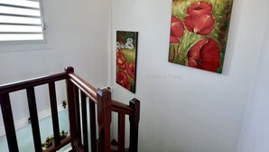 A staircase with wooden railings leading to a landing where two paintings of red flowers are displayed on the wall.