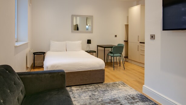 A modern hotel room with a bed, a small desk, a chair, and a television. - Charles Hope Apartments Swindon (Swindon)
