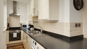 A modern kitchen with white cabinets, a black countertop, stainless steel appliances, and a clock on the wall. - Charles Hope Apartments Swindon (Swindon)