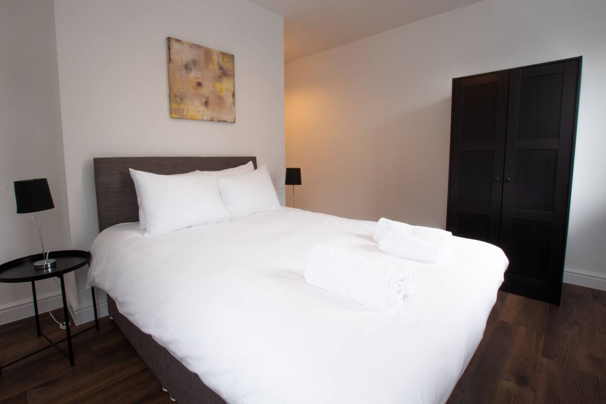A neatly made bed with white linens, a dark headboard, and two bedside lamps.