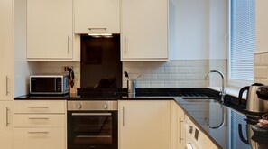 A modern kitchen with white cabinets, a microwave, an oven, and a sink. - Charles Hope Apartments Swindon (Swindon)