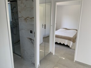 Ein modernes Badezimmer mit Duschkabine aus Glas, Marmorplatten an der Wand und einem Bett mit gesteppter Decke.
