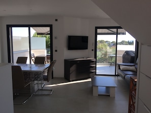Ein modernes Wohnzimmer mit Flachbildfernseher, Essbereich mit Tisch und Stühlen sowie einer Couch.