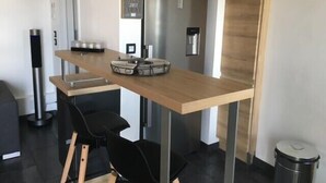 Ett modernt kök med en bänkskiva i trä, svarta stolar, en kaffemaskin och ett kylskåp i rostfritt stål.